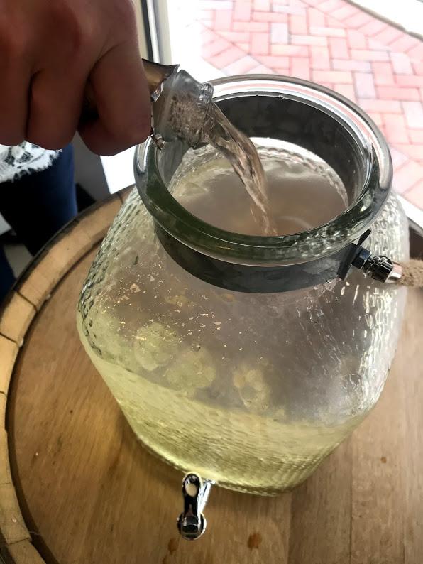 pouring white wine into pitcher for Sparkling Peach Sangria recipe directions
