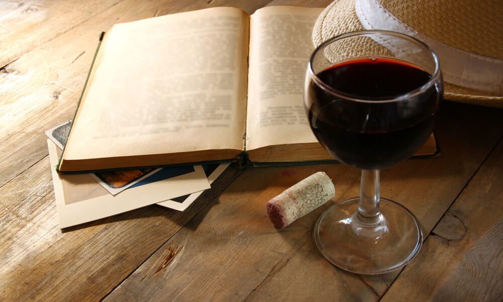 glass of red wine next to open book and cork
